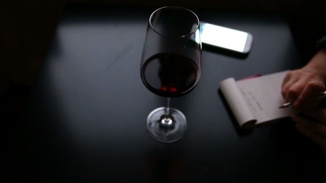 person working and taking notes with a glass of wine at home and smartphone to connect on internet