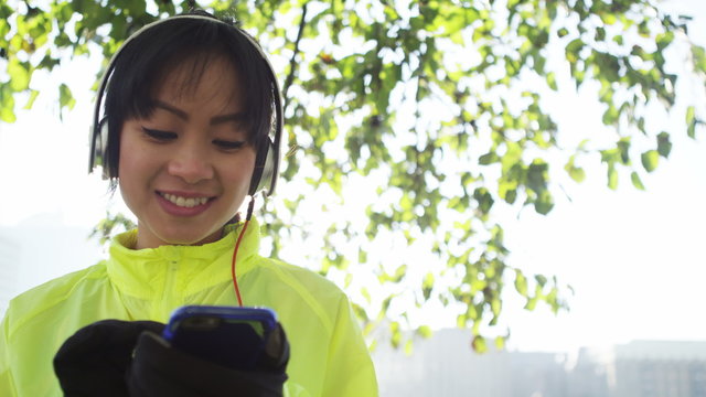  Attractive asian woman listening to music on her phone working out outdoors