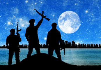 Silhouette of men with rifle standing against city at night