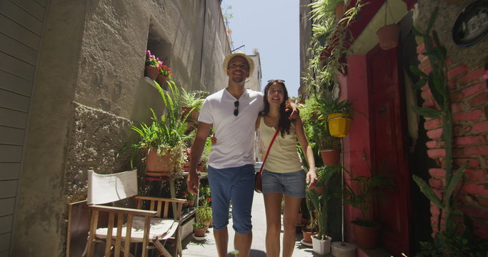  Attractive couple on vacation walking through narrow city alley with lots of plants. 
