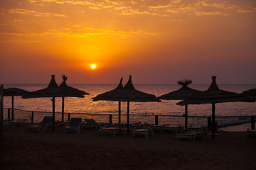 Vacation holidays background wallpaper -  beach lounge chairs under tents on beach. Egypt hotel Sharm El Sheikh at sunset