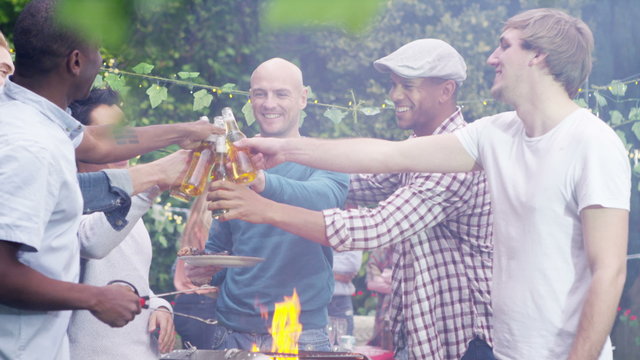  Happy mixed ethnicity group of male friends chatting & drinking beer at bbq