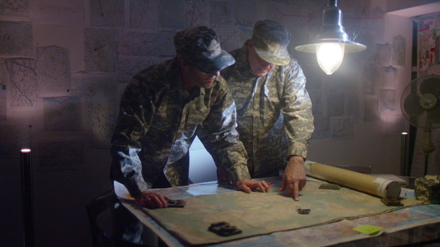  Military officers in army bunker, looking at map & discussing battle strategy
