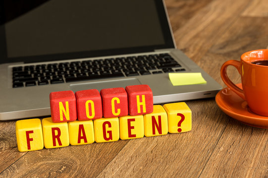 Any Question? (in German) written on a wooden cube in a office desk