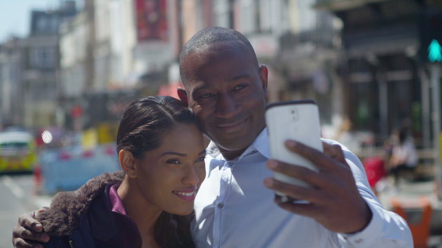  Happy attractive couple in the city taking a selfie with camera phone.