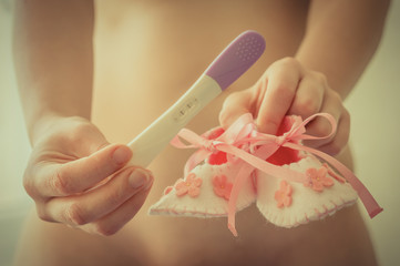 Young woman holding baby shoes and pregnancy test