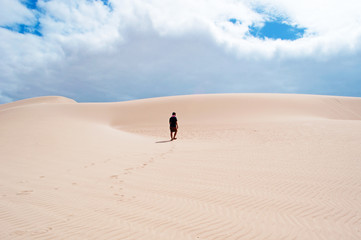 Fototapeta na wymiar Un uomo cammina sulle dune di sabbia di Stero, nell'area protetta della spiaggia di Aomak, isola di Socotra, Yemen