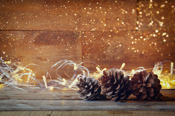 pine cones next to gold garland lights on wooden background. copy space
