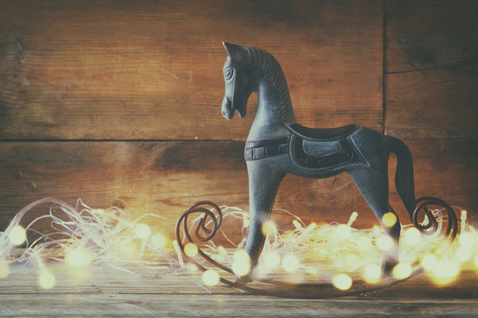 double exposure image of rocking horse and magic christmas lights on wooden table