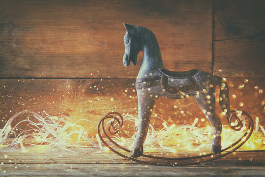 double exposure image of rocking horse and magic christmas lights on wooden table