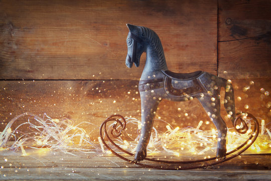 double exposure image of rocking horse and magic christmas lights on wooden table