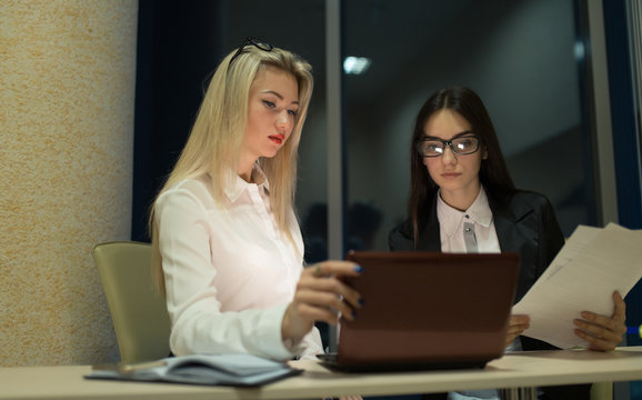 Two businesswomen working with a laptop in office late at night