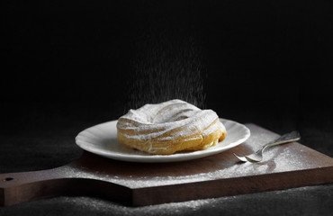 Tart with a fall of powdered sugar on wooden cutting board and black background