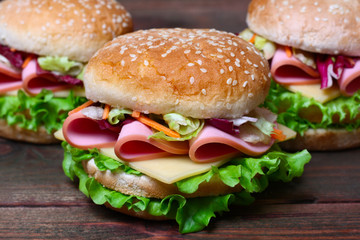 Burger sandwich with sausage, cheese and vegetables on a wooden background