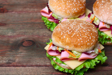 Burger sandwich with sausage, cheese and vegetables on a wooden background