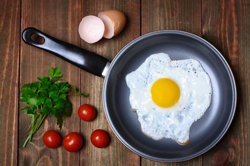 Pan of fried eggs, with cherry-tomatoes and parsley on a wooden table surface