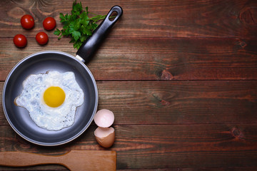 Pan of fried eggs, with cherry-tomatoes and parsley on a wooden table surface