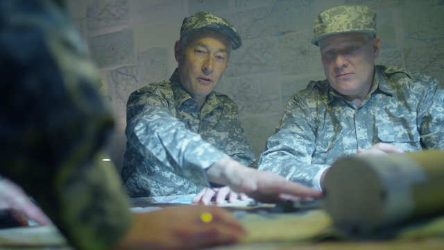  Military officers in army bunker, looking at map & discussing battle strategy
