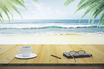Fototapeta na wymiar Wooden table with cup of coffee, eyeglasses and diary on the bea