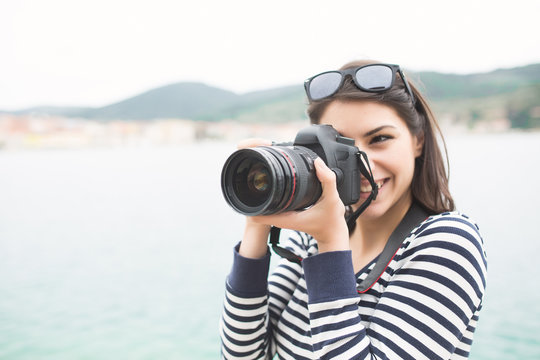 Happy woman on vacation photographing with a dslr camera on the beach and smiling