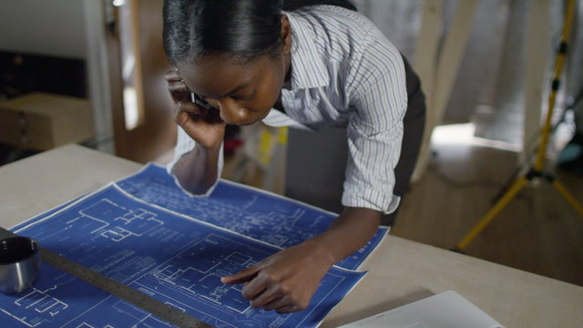  Confident female engineer or architect talking on phone and looking at construction plans. 
