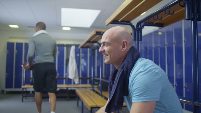  Portrait of man in gym locker room, he high fives another man passing by