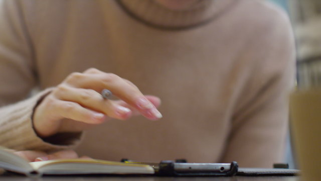  Hands of woman writing in her diary and using a smart phone at cafe