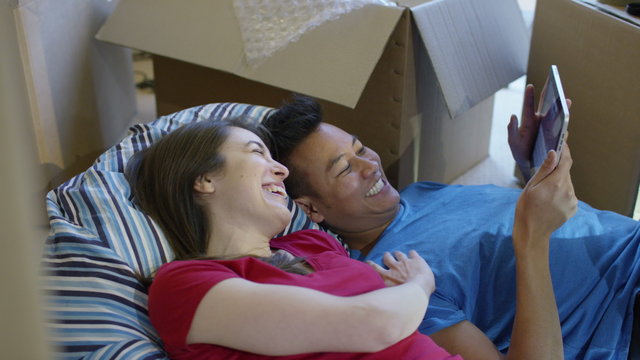  Happy young couple with computer tablet, lying on floor in new home