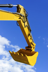 Excavator bucket, bulldozer shovel, hydraulic piston system of yellow construction vehicle isolated on blue sky with white clouds  © antonmatveev