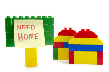 two home icon made from plastic building blocks and signage with handwriting word "need home" on yellow sticky paper. isolated on white background