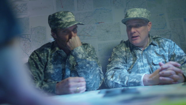  Military officers in army bunker, looking at map & discussing battle strategy