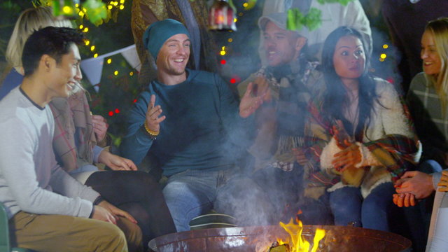  Happy mixed ethnicity friends socializing outdoors in front of fire pit