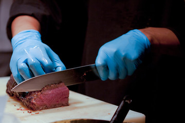 Butcher Cutting Medium Rare Beef on Cutting Board in the Kitchen