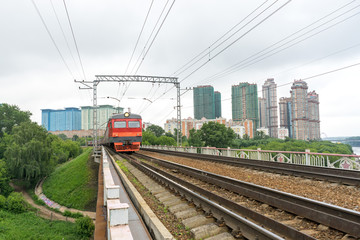 Obraz premium Red and grey suburban electric train moves towards on railroad turn vanishing against skyline background. Moscow, Russia. 