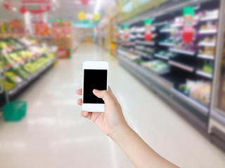 Hand holding mobile phone with Vegetables and fruit on shelf