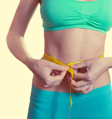 Fit and healthy young woman measuring her waist with a tape measure. Isolated.