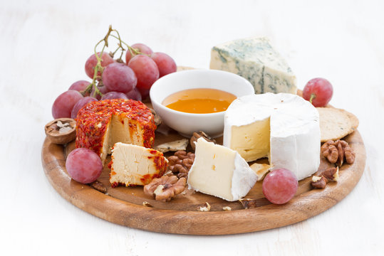 cheeses and snacks on a wooden board on white table