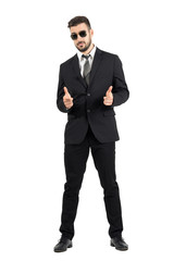 Secret agent with sunglasses aiming hand gun gesture at camera. Full body length portrait isolated over white studio background.