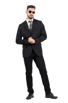 Businessman with sunglasses holding clasped hands. Full body length portrait isolated over white studio background.