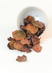      Thin round beetroot chips baked in the oven with oregano and salt poured out of a bowl in white background. A healthy, vegetarian, vegan, crispy snack appetiser for diet and clean eating.