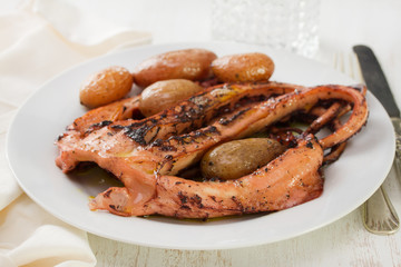 boiled octopus with potato on plate on white wooden background