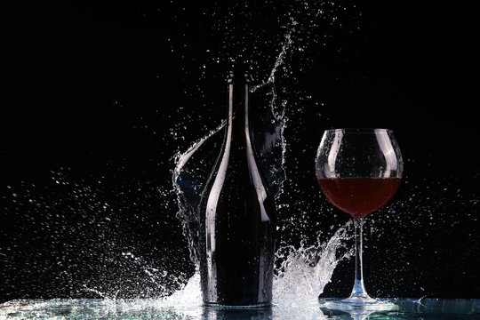 Bottle With Red Wine, Water Splash, Wine On Table On Black Background, Big Splash Around Bottle Of Red Wine