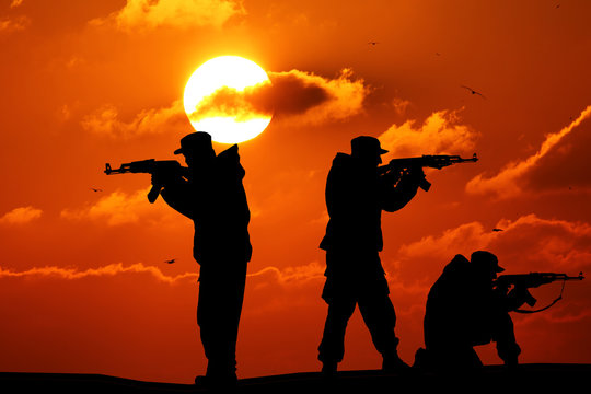 Silhouette of military three soldier or officer with weapons at sunset. shot, holding gun, colorful sky, mountain, background, team