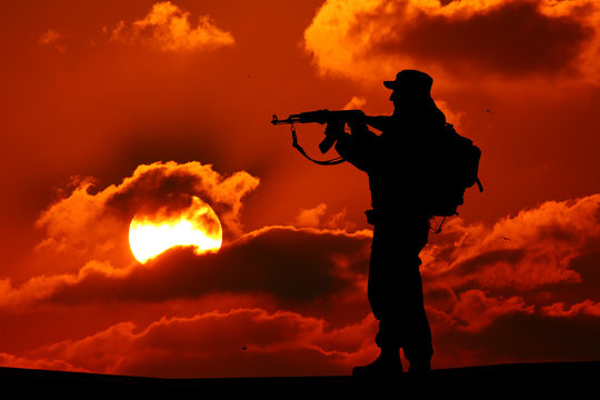 Silhouette of military soldier or officer with weapons at sunset. shot, holding gun, colorful sky, mountain, background