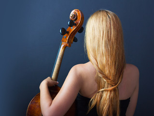 Beautiful girl with a cello on a black background. Cellist. Girl musician.
