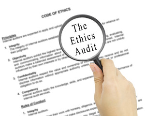Magnifying glass with word THE ETHICS AUDIT in hand