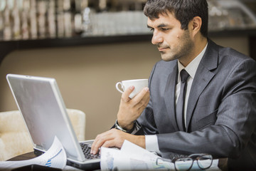 Бизнесмен в деловом костюме работает за компьютером и пьет кофе.