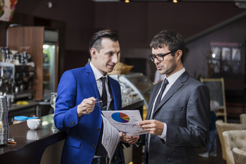 Бизнесмен в кафе разговаривает с инвестором, который держит в руках документы и графики 