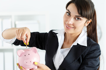 Obraz na płótnie Canvas Happy beautiful woman putting pin money coins into pink piggyban