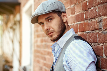 casual young man stands with his back against brick wall 